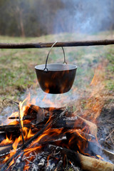 Outdoor camping - cooking food on campfire in forest. Cauldron on fire in nature