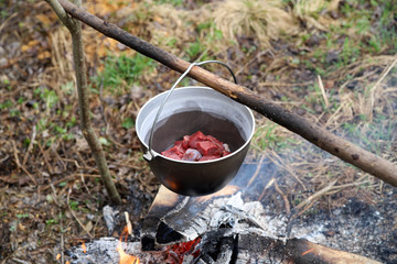 Cooking meat in a cauldron on a campfire. Food in outdoor. Life in nature