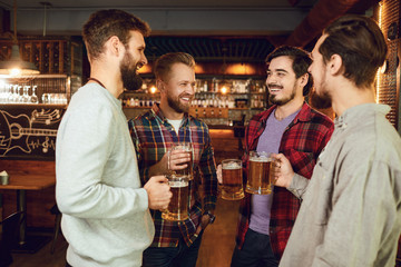Group of happy friends clinking glasses with beer at a sports bar.