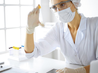 Professional female scientist in protective eyeglasses researching tube with reagents in...
