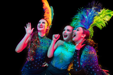 Celebrate. Beautiful young women in carnival, stylish masquerade costume with feathers on black background in neon light. Copyspace for ad. Holidays celebration, dancing, fashion. Festive time, party. © master1305