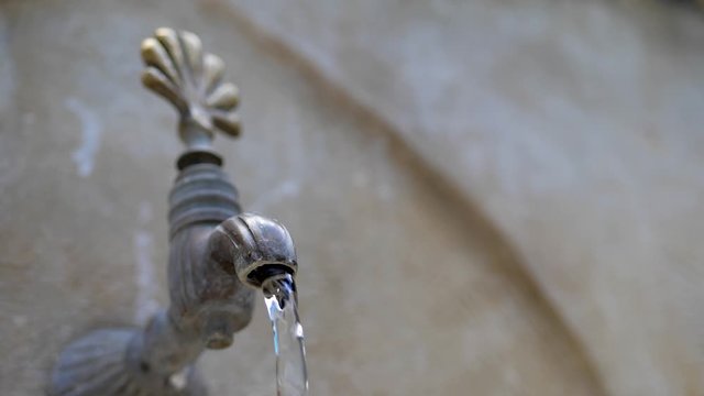 Water flows from an old stone crane in oriental style. close-up