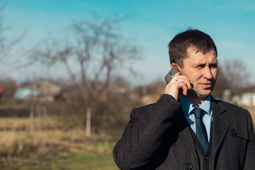 a middle-aged businessman man talking on the phone against a rural landscape on a Sunny day