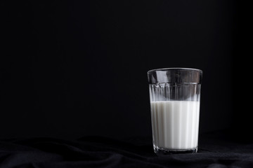 One glass with milk on a black background