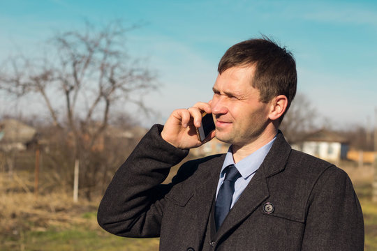 a middle-aged businessman man talking on the phone against a rural landscape on a Sunny day