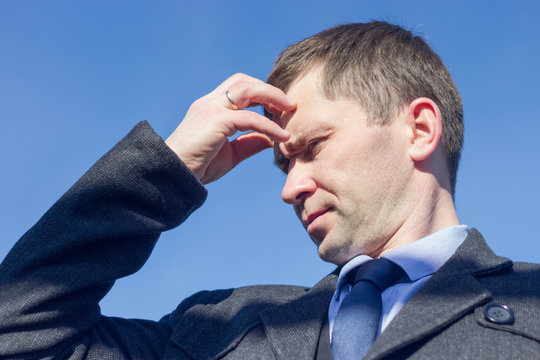 portrait of a man in a coat with a thoughtful look against the blue sky, holding his head with one hand (portrait of the Creator)