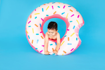 Happy baby boy in swimsuit with swimming ring donut on a colored blue background