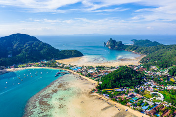 Flying above busy tropical island port filled with boats and ferries. Countless ships sail to and from bustling harbor on exotic beach. Picturesque shot of fleet of anchored longtail boats.