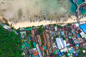 Flying above busy tropical island port filled with boats and ferries. Countless ships sail to and from bustling harbor on exotic beach. Picturesque shot of fleet of anchored longtail boats.