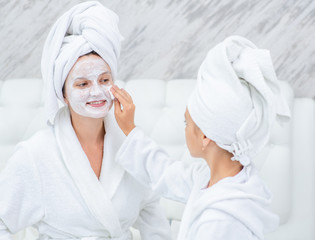 Little girl cleans her mom's face with a cotton pad and lotion