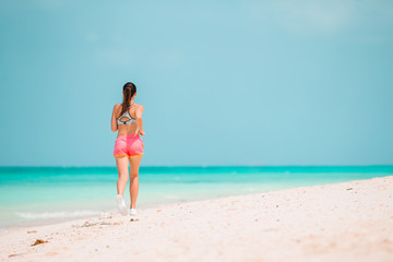 Fototapeta na wymiar Fit young woman doing exercises on tropical white beach in her sportswear