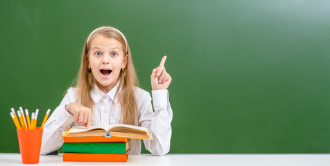 Very happy girl with books points away on empty school board. Empty space for text