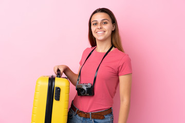 Teenager traveler girl holding a suitcase over isolated pink background smiling a lot