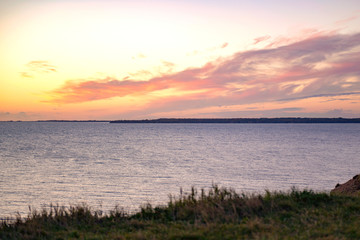 Naklejka premium Bright yellow colors of sunset sky under the sea. Beautiful sunrise at sea. The sea in the foreground. A bright beautiful yellow sun in the sky illuminates clouds and sea waves in orange sea sunset