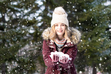 Young blonde woman in winter park having fun with snow falling in hands