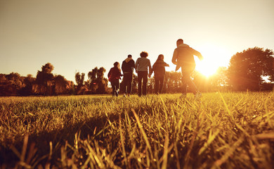 A group of young people running through the grass in the park at sunset.