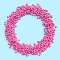 Pink coated chocolate candies arranged in circle frame on blue pastel background