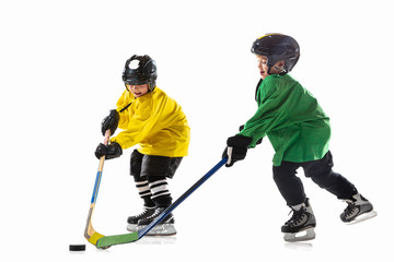 Fototapeta premium Little hockey players with the sticks on ice court and white studio background. Sportsboys wearing equipment and helmet practicing. Concept of sport, healthy lifestyle, motion, movement, action.