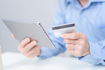 Hands of an elderly person hold credit card and use tablet computer. Online shopping