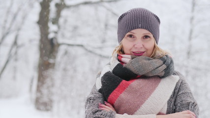 A woman in a warm sweater and a bright scarf stands in a snow park