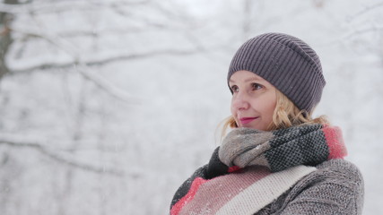 Side view of A woman in a warm sweater and a bright scarf stands in a snow park