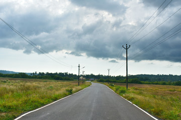 Fototapeta premium Beautiful Empty road in Autumn season with green fields and cloudy sky in Goa