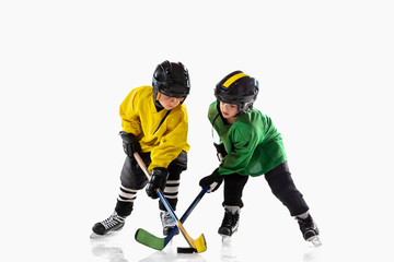Little hockey players with the sticks on ice court and white studio background. Sportsboys wearing equipment and helmet practicing. Concept of sport, healthy lifestyle, motion, movement, action.