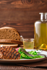 Grilled beef cutlet with fresh salad, brown bread and moonshine on rustic wooden table