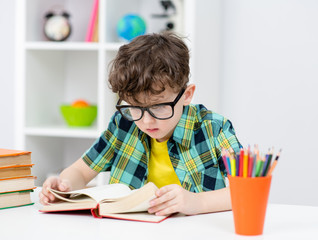 Smart boy wearing a eyeglasses reads book at home