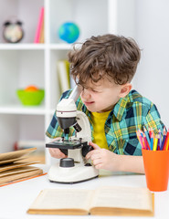 Young boy doing a homework and uses the microscope