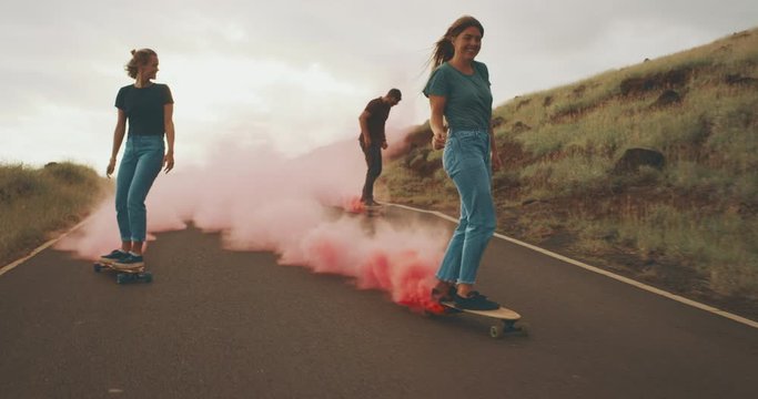 Three young adventurous friends skateboarding together with colorful pink smoke trails, stylish millennials riding skateboards with funky fun pink smoke