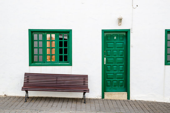 Green door window and seating bank wooden made in a white facade.