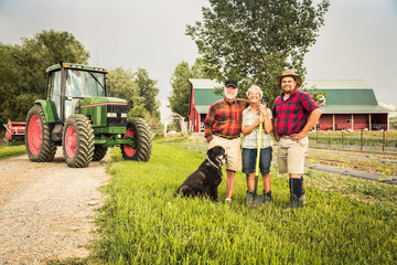 Portrait of farming family laughing after long day of work with dag, tractor and barn. Laurel, Montana, USA