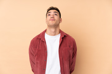 Young caucasian handsome man isolated on beige background and looking up