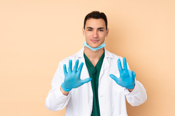 Young dentist man holding tools isolated on beige background counting eight with fingers