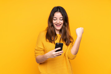 Young caucasian woman isolated on yellow background with phone in victory position