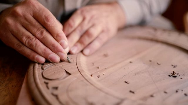 Expert craftsman work on his beautiful wood ornamental plate. Slowmotion closeup shot of a master craftsman doing traditional wood carving