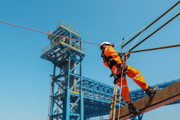 Safety man worker sprinkle, ropeaccess from structure steel with safety harness and wearing equipment protective PPE on blue sky background - obrazy, fototapety, plakaty