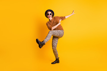 Full size photo of funky lady raise leg high rejoice vacation student youth party celebrating wear soft sweater leopard pants specs retro cap shoes isolated yellow color background