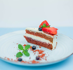 A beautiful piece of cake with berries with butter cream on a blue background. Cake with red cakes.