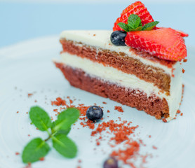 A beautiful piece of cake with berries with butter cream on a blue background. Cake with red cakes.