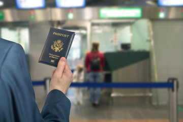 Man (businessman)  in a blue suit with suitcase holding american passport with boarding pass in the airport opposite Immigration and passport control. concept. America. USA