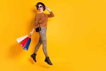 Full length photo of funky lady jump high sales shopping carry packs black friday wear fluffy pullover leopard pants shoes retro cap clutch specs isolated yellow color background