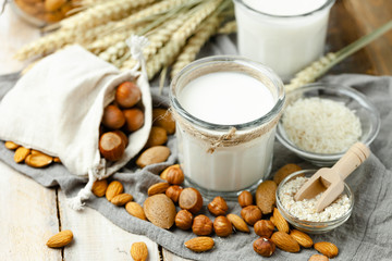 Fresh vegan alternative milk in big glass. Closeup, wooden background. Healthy vegetarian food concept, delicious low calorie drink. Almond, hazelnut, oatmeal, rice to illustrate raw ingredients. 