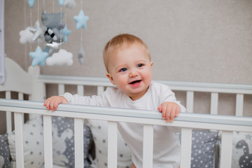 healthy baby in white clothes is sitting in a child's bed