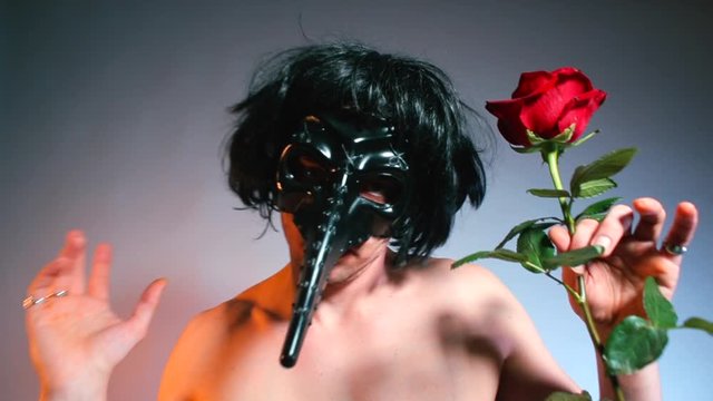 A man in a mask and with a rose in his hands makes dance moves at a kinky party