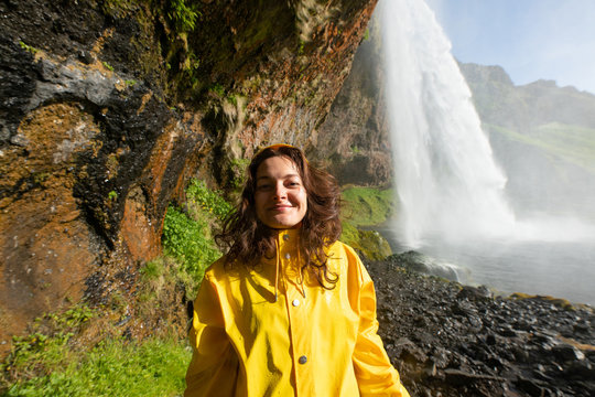 Happy Young Woman In Yellow Jacket Posing Under Seljalandfoss Waterfall