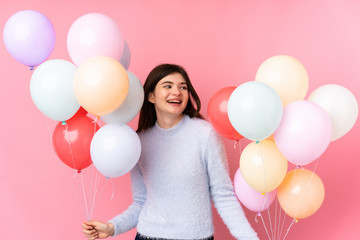 Young Ukrainian teenager girl holding lots of balloons over isolated pink background