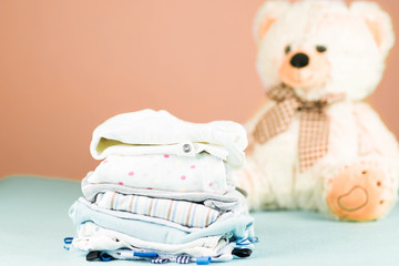 fresh washed and ironed baby clothes neatly folded on pink background with a teddy bear