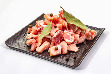 Diced raw pork meat, isolated on white background. Fresh pieces, dry bay leaf on black ceramic plate
